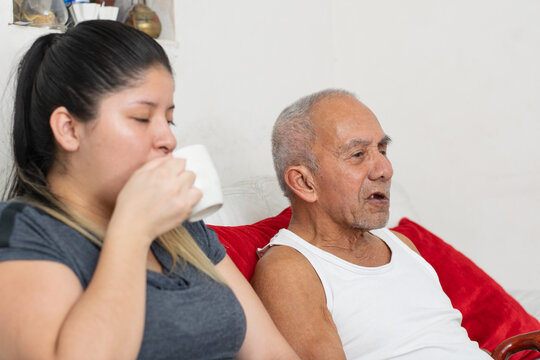 Young woman sipping coffee while talking with elderly grandfather creating warm family interaction