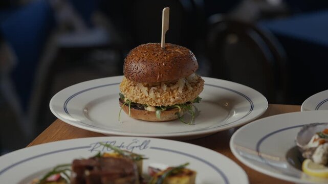 Burger sits on a plate, ready to be enjoyed. Wooden toothpick holds it together neatly. Table shows multiple dishes, adding to the meal's variety. Dinner scene suggests comfort and casual dining