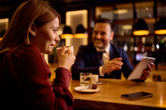 Smiling entrepreneur drinking coffee while using touchpad with her colleague in cafe.