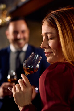 Smiling woman tasting cognac while drinking in bar.