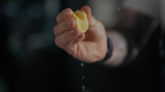 Hand squeezes lemon, juice drips slowly. Dark background highlights the vibrant yellow fruit. Close-up captures freshness, zesty essence. Ideal for food, beverage, or wellness projects