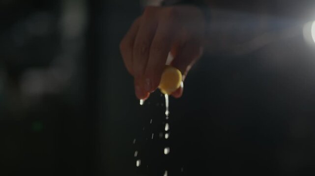 Hand squeezes lemon, juice drips down. Light flares behind, casting shadows. Close-up, slow-motion, captures freshness. Use for food, health, or natural product visuals