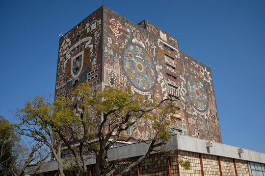 The building displays vibrant mural art on its exterior under clear sky, located in Universidad Nacional Aut&oacute;noma de M&eacute;xico - UNAM - representing academic and cultural heritage.