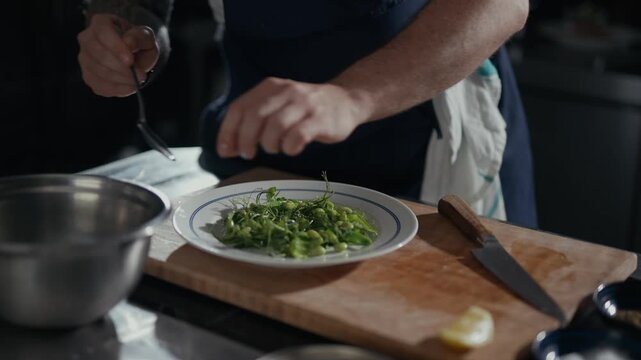 Chef prepares fresh greens with care and precision. Hands mix herbs gently on a clean plate. Kitchen tools and ingredients surround the action. Perfect for food, wellness, or culinary tutorials