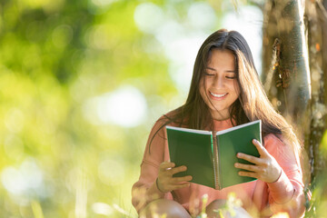 Fototapeta premium Young woman smiling while reading book outdoors in nature