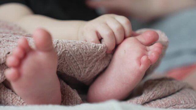 Baby feet and hands wrapped in soft pink knit blanket showing tiny toes and delicate fingers in closeup. Newborn infant resting peacefully with small foot and hand visible through cozy textile wrap.