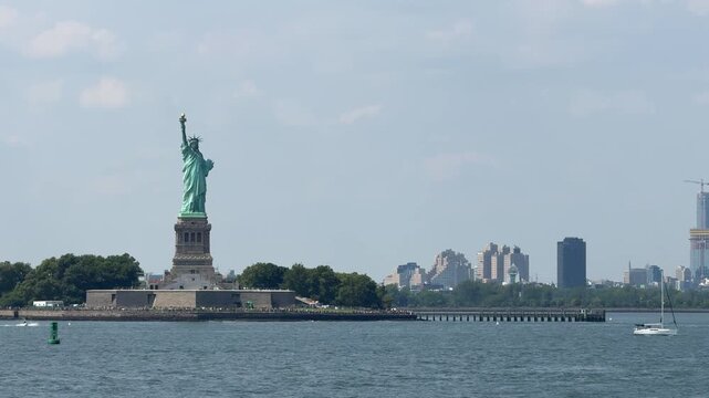 Long-distance view of the Statue of Liberty across open harbor water with soft city skyline in the background. Minimal peaceful composition emphasizes scale, space, and iconic American scenery.