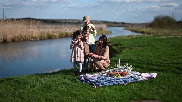 A Family Enjoys a Beautiful Spring Picnic by the River, Sharing Happy Moments and Healthy Food in the Serene Outdoors on a Sunny Day