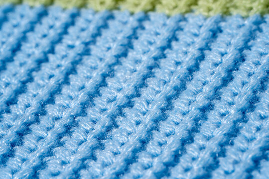 Close-up sweater texture in blue color knit with green stripe, showing macro stitch detail and synthetic material surface. Concept of practical knitwear, durable textile and easy-care wardrobe