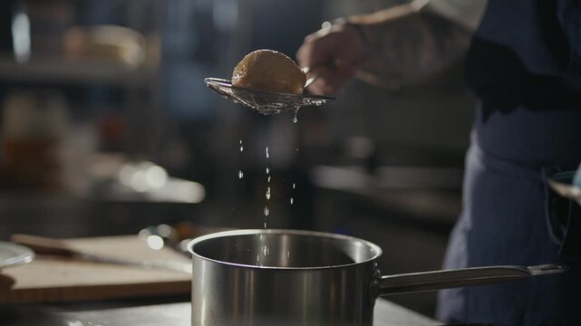 Cooking pot steams as a hand lifts a round food item. Steam curls from the pot, indicating heat and active preparation. The chef's focused expression suggests precision and care