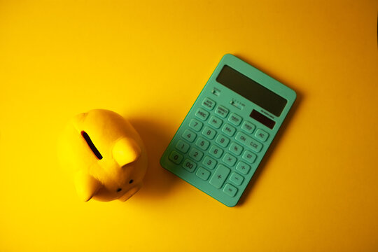 Calculator and piggy bank on yellow background, top view