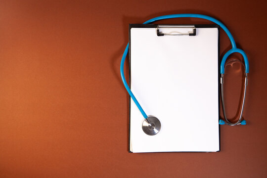 Stethoscope and blank paper on brown background with copy space.
