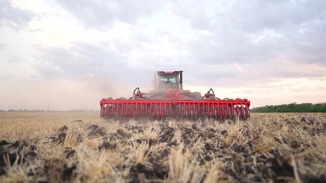 Tractor cultivating field with disc harrow farming equipment during cultivation season. Agricultural machinery working on farmland. Tractor tilling soil. Farm cultivation process in field.