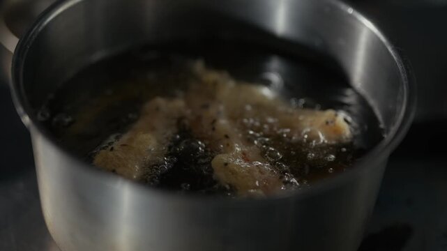 Hot oil bubbles in metal pot. Metal spoon stirs contents gently. Food sizzles, turning golden brown. Cooking scene, warm, active. Use for food, cooking, kitchen, restaurant, or culinary content