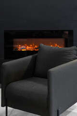 Naklejka premium Elegant dark grey armchair near fireplace. Modern home relaxation area interior design.