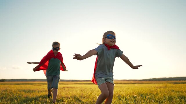 Children playing superhero running field sunset wearing cape mask. Kids pretend superheroes outdoors. Boy girl run with cape in meadow. Children play hero game at sunset wearing mask cape field.