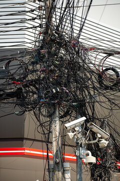 Abundance of wires in Asia, messy tangled electricity wires and data cables on pole, typical asian urban landmark, mixed cables and wires on pole with video surveillance pole at street in city.