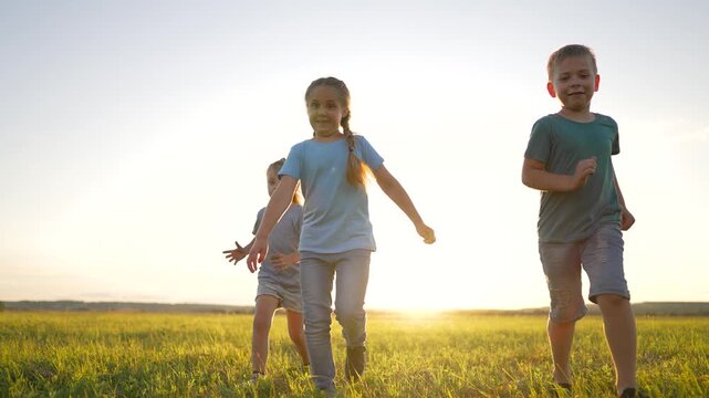 Children playing soccer in grass field at sunset. Happy kids kick football ball outdoors. Three siblings run with soccer in green meadow. Boy and girls play football during golden hour sunlight.