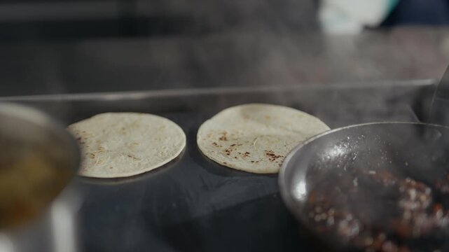 Steam rises from a hot griddle. Hands place tortillas carefully on the surface. Cooking process is shown with precision. Tortillas sizzle, creating a warm, aromatic scene. Ideal for food, restaurant