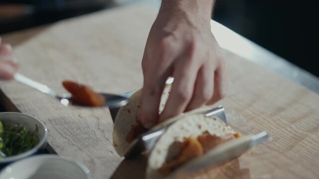 Hand places filling into a tortilla. Fingers gently guide ingredients onto soft bread. Close-up captures careful, deliberate motion. Perfect for food prep or casual dining scenes