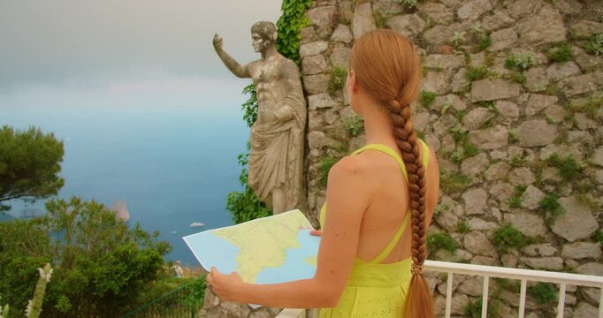 Woman holding a map near ancient statue of Emperor Augustus overlooking sea and Faraglioni stacks on Capri island