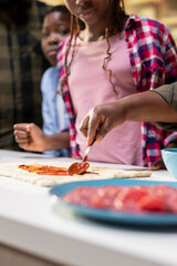 Fototapeta premium Close up of young kids spreading tomato sauce on pizza dough at home, making homemade meal with fresh ingredients and produce. Adding dressing as first step, family time in the kitchen.