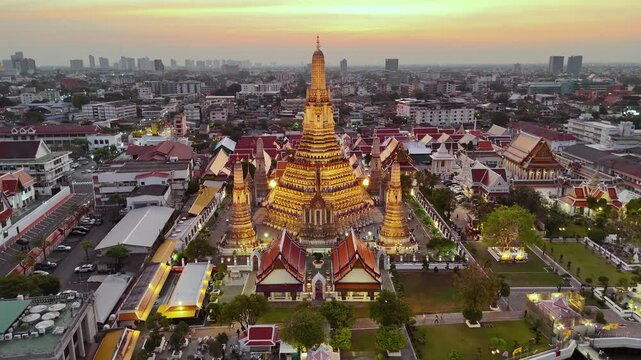 Aerial drone view of the famous Wat Arun temple also known as the Temple of Dawn, stands tall by the river Chao Phraya at night in Bangkok reflects the vibrant hues of the sunset against the cityscape