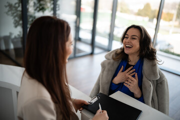 Obraz premium Two women laughing and talking at reception desk