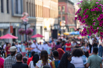 Obraz premium Crowd of people gathering on busy city street during summer festival. Sparks street in Ottawa, Canada. Blurred urban scene with people and flowers in foreground