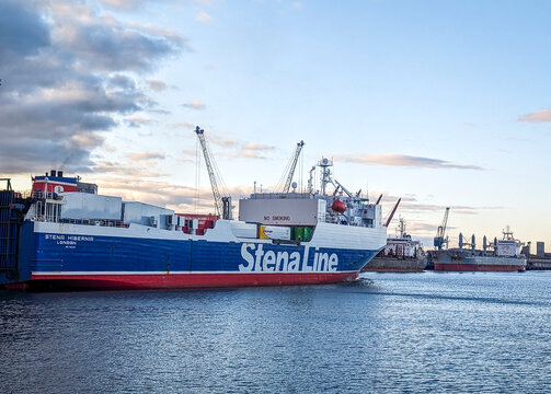 Belfast, UK, June 14, 2024. View of a Stena Line cargo ship carrying freight departs Belfast Harbour against a vibrant sunset sky.