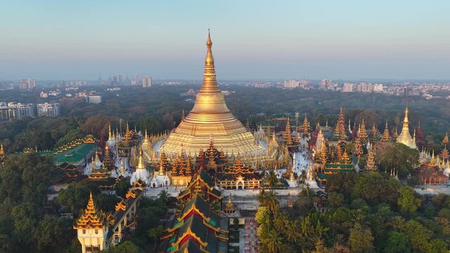 Aerial drone view at Shwedagon Pagoda, a golden stupa, surrounded by lush greenery and urban development in Yangon (Rangun), Myanmar (Burma), showcasing the city's blend of religious and modern life.