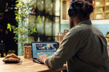 Obraz premium Man editing video clips and sound effects with headset at laptop, videography and post production with cinematic color grading. VFX elements and interactive software, professional content creator.