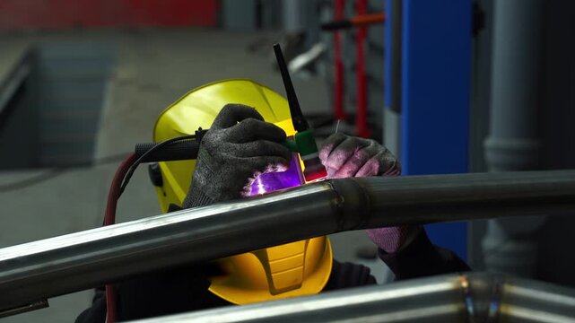 4k video Worker performs TIG welding on metal using a tungsten electrode with argon shielding gas, wearing a protective welding helmet for safety.