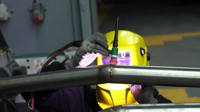 4k video Welder performs argon TIG welding on a custom automotive exhaust pipe using a tungsten electrode for precise fusion, wearing a protective welding helmet.
