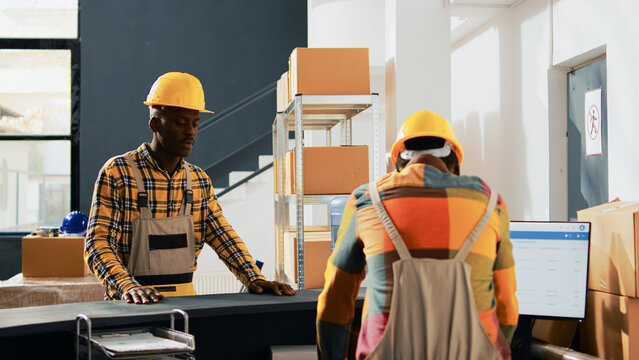 African american employees doing fist bump gesture in warehouse, greeting each other at work. Team of men working in storage room with containers and boxes of merchandise. Handheld shot.