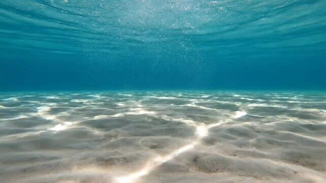 Underwater view of clear blue water with bubbles and sand