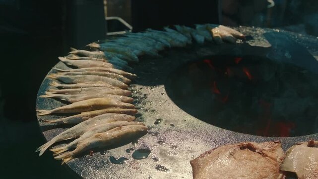 Fresh fish grilling on a hot metal plate over an open fire. Assorted seafood cooking on a barbecue. Traditional outdoor street food preparation and rustic summer picnic cooking concept.