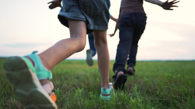 Children running freely across green field at sunset, arms outstretched wide. Kids run together through grass, viewed from low angle. Child group enjoys outdoor freedom. Kids play in summer field.