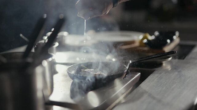 Smoke curls from a hot pan. Chef's hand pours liquid with precise motion. Metal surfaces gleam under focused light. Steam rises, hinting at flavor in motion