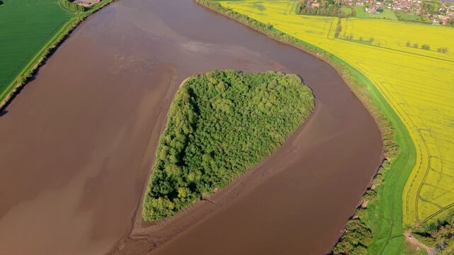 Aerial view of Howden Dyke Island in the River Ouse surrounded by vibrant yellow rapeseed fields and green meadows in Goole, England, United Kingdom.