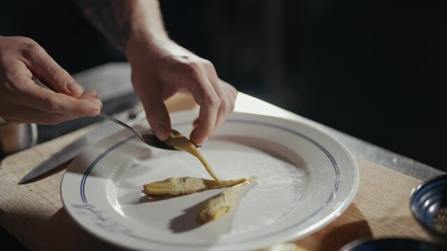 Hands gently place food on a white plate. Tender fingers work with care and precision. Kitchen setting suggests a quiet, thoughtful meal. Ideal for culinary or food preparation scenes