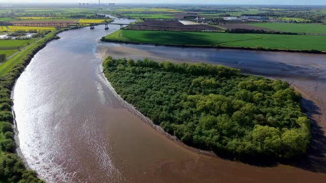 Aerial view of Howden Dyke Island on the River Ouse with lush green trees and muddy banks near Goole, England, United Kingdom.
