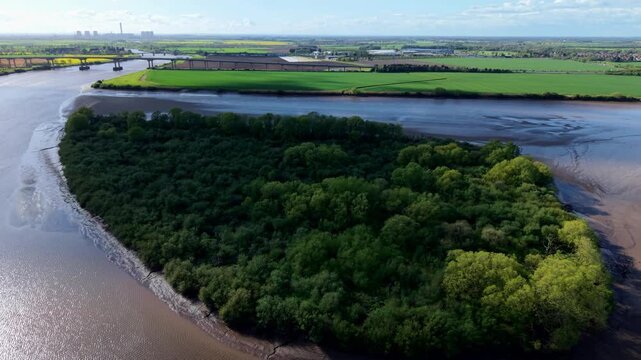 Aerial view of Howden Dyke Island in the River Ouse with the M62 bridge and green fields under a blue sky in Goole, England, United Kingdom.