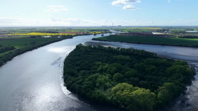 Aerial view of Howden Dyke Island on the River Ouse with the M62 bridge and industrial chimneys in the distance under a bright sky Goole, England, United Kingdom.