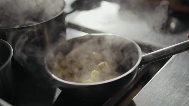 Steam rises from a pan of sauteing onions. Pot steams on the stove behind it. Hand grips the pan's handle. Heat and flavor simmer in the kitchen. This scene evokes comfort and home cooking