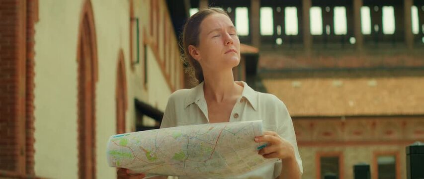 Woman squinting at a map and overlooking sunlit alley with historic buildings