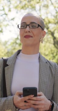 Businesswoman, walk and smile in park with phone, text message or morning commute for real estate job. Happy, female person and realtor thinking outdoor with digital tech, glasses and travel to work.