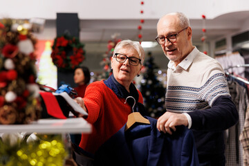 Fototapeta premium Senior people checking ties on display at mall retail boutique, looking for formal clothes to wear on christmas eve dinner. Man and woman clients searching for elegant items in festive shop.