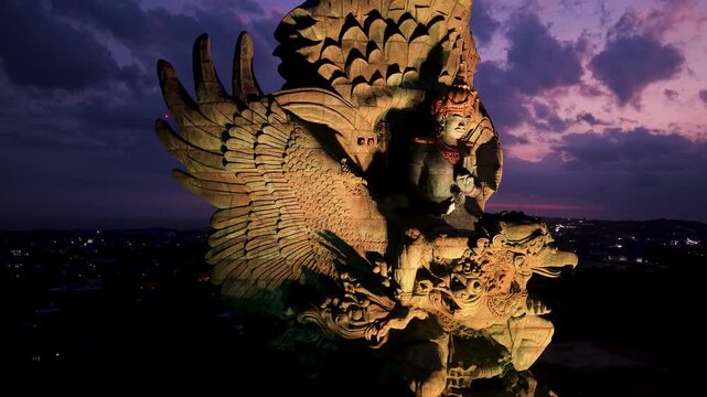 Aerial view of the illuminated Garuda Wisnu Kencana statue under a purple twilight sky in Kecamatan Kuta Selatan, Bali, Indonesia.