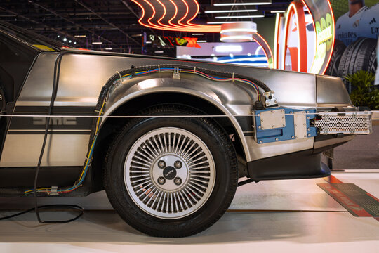 Side detail of a DeLorean DMC-12 showing stainless steel body, turbine wheel, exposed wiring harness, and industrial finish.